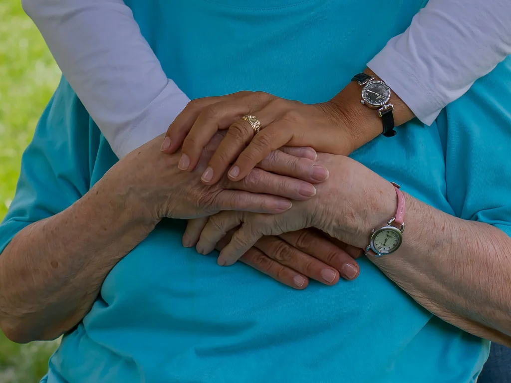 Caregiver holding elderly resident's hands to provide comfort and support